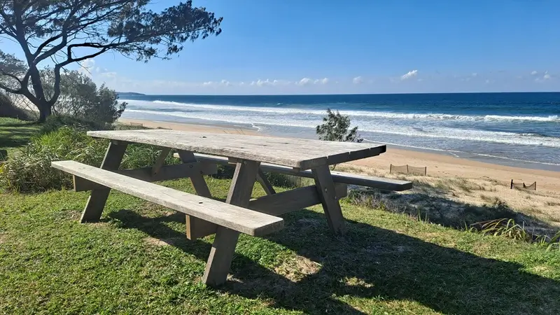 Weathered Billabong hardwood picnic table beside an exposed beach