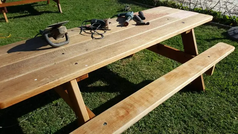 Sanding tools on a weathered hardwood picnic table during restoration